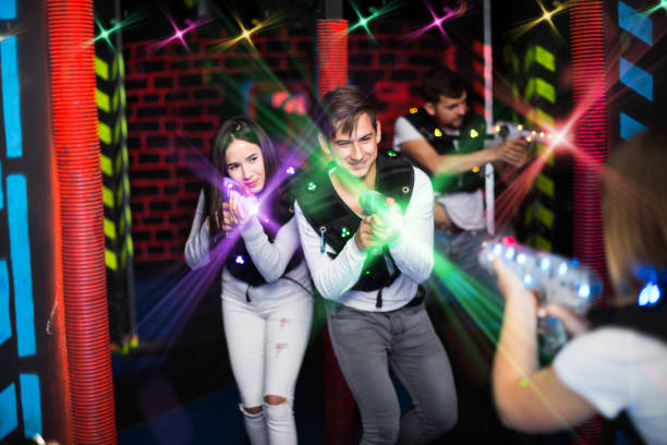 Young couple playing laser tag with friends in labyrinth illuminated by bright beams of laser guns